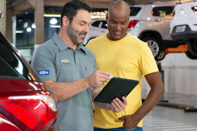 Duas pessoas na oficina Chevrolet verificando a lista de reparos concluídos em um Tablet